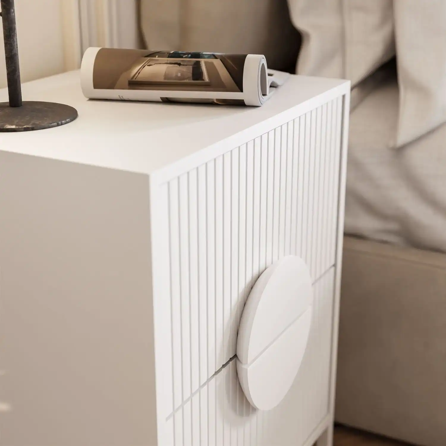 naktinis staliukas su grioveliuotu priekiu Baltos spalvos LUNO naktinis staliukas šiuolaikiniame miegamajame su minimalistiniu dekoru.